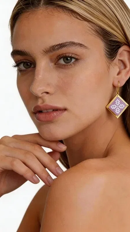 , These statement embroidered earrings in a soft lilac shade with geometric patterns in gold thread are the perfect choice for adding a touch of elegance and originality to your look. Designed by Greek Jewelry Designer Aikaterini Chalkiadaki, these handmade earrings combine the traditional technique of embroidery with contemporary design. Their square geometric shape is adorned with intricately embroidered motifs in a soft lilac tone, while the gold outline adds a luxurious touch. The folklore design with its detailed geometric patterns creates a unique piece of jewelry that stands out and complements both casual and formal looks. Ideal for women who love statement accessories, these earrings are perfect for special occasions, weddings, or for adding a splash of color to your everyday style.

Material: Brass, Fabric. To care for them, store the earrings in a dry place and avoid contact with water and chemicals.