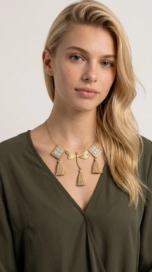 , The statement embroidered ivory necklace with geometric designs is a handmade piece that combines the traditional art of embroidery with a modern aesthetic, creating a result that instantly catches the eye. Designed by Greek Jewelry Designer Aikaterini Chalkiadaki, it is a tribute to folk art and Greek craftsmanship.

The necklace features gold-toned geometric brass elements in a diamond shape, adorned with delicate embroidered motifs in an ivory hue, evoking the rich aesthetic vocabulary of folklore. Among them, a gold metallic dragonfly-shaped element adds grace and movement to the piece. Three fabric tassels in an ivory-beige shade hang elegantly, giving depth and motion to the jewelry.

Ideal for summer outfits, boho and ethnic looks, as well as for elevating a simple dress or blouse. It pairs perfectly with linen clothing, maxi dresses, or casual summer looks.