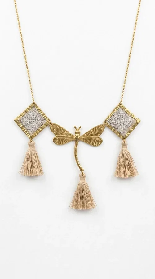 , The statement embroidered ivory necklace with geometric designs is a handmade piece that combines the traditional art of embroidery with a modern aesthetic, creating a result that instantly catches the eye. Designed by Greek Jewelry Designer Aikaterini Chalkiadaki, it is a tribute to folk art and Greek craftsmanship.

The necklace features gold-toned geometric brass elements in a diamond shape, adorned with delicate embroidered motifs in an ivory hue, evoking the rich aesthetic vocabulary of folklore. Among them, a gold metallic dragonfly-shaped element adds grace and movement to the piece. Three fabric tassels in an ivory-beige shade hang elegantly, giving depth and motion to the jewelry.

Ideal for summer outfits, boho and ethnic looks, as well as for elevating a simple dress or blouse. It pairs perfectly with linen clothing, maxi dresses, or casual summer looks.