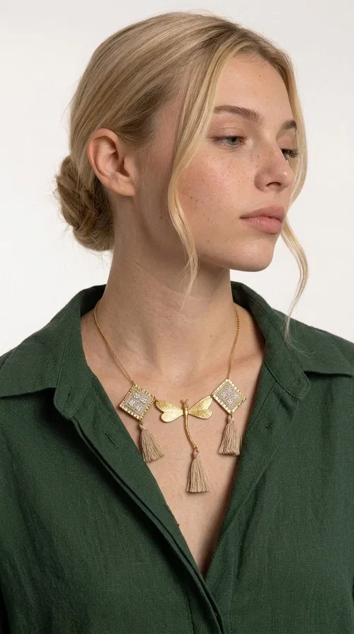 , The statement embroidered ivory necklace with geometric designs is a handmade piece that combines the traditional art of embroidery with a modern aesthetic, creating a result that instantly catches the eye. Designed by Greek Jewelry Designer Aikaterini Chalkiadaki, it is a tribute to folk art and Greek craftsmanship.

The necklace features gold-toned geometric brass elements in a diamond shape, adorned with delicate embroidered motifs in an ivory hue, evoking the rich aesthetic vocabulary of folklore. Among them, a gold metallic dragonfly-shaped element adds grace and movement to the piece. Three fabric tassels in an ivory-beige shade hang elegantly, giving depth and motion to the jewelry.

Ideal for summer outfits, boho and ethnic looks, as well as for elevating a simple dress or blouse. It pairs perfectly with linen clothing, maxi dresses, or casual summer looks.