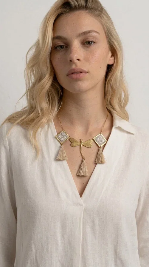, The statement embroidered ivory necklace with geometric designs is a handmade piece that combines the traditional art of embroidery with a modern aesthetic, creating a result that instantly catches the eye. Designed by Greek Jewelry Designer Aikaterini Chalkiadaki, it is a tribute to folk art and Greek craftsmanship.

The necklace features gold-toned geometric brass elements in a diamond shape, adorned with delicate embroidered motifs in an ivory hue, evoking the rich aesthetic vocabulary of folklore. Among them, a gold metallic dragonfly-shaped element adds grace and movement to the piece. Three fabric tassels in an ivory-beige shade hang elegantly, giving depth and motion to the jewelry.

Ideal for summer outfits, boho and ethnic looks, as well as for elevating a simple dress or blouse. It pairs perfectly with linen clothing, maxi dresses, or casual summer looks.
