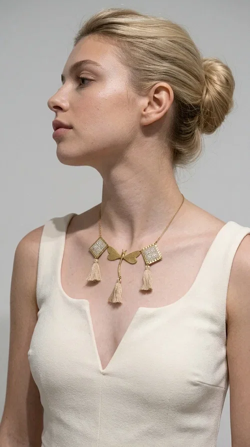 , The statement embroidered ivory necklace with geometric designs is a handmade piece that combines the traditional art of embroidery with a modern aesthetic, creating a result that instantly catches the eye. Designed by Greek Jewelry Designer Aikaterini Chalkiadaki, it is a tribute to folk art and Greek craftsmanship.

The necklace features gold-toned geometric brass elements in a diamond shape, adorned with delicate embroidered motifs in an ivory hue, evoking the rich aesthetic vocabulary of folklore. Among them, a gold metallic dragonfly-shaped element adds grace and movement to the piece. Three fabric tassels in an ivory-beige shade hang elegantly, giving depth and motion to the jewelry.

Ideal for summer outfits, boho and ethnic looks, as well as for elevating a simple dress or blouse. It pairs perfectly with linen clothing, maxi dresses, or casual summer looks.