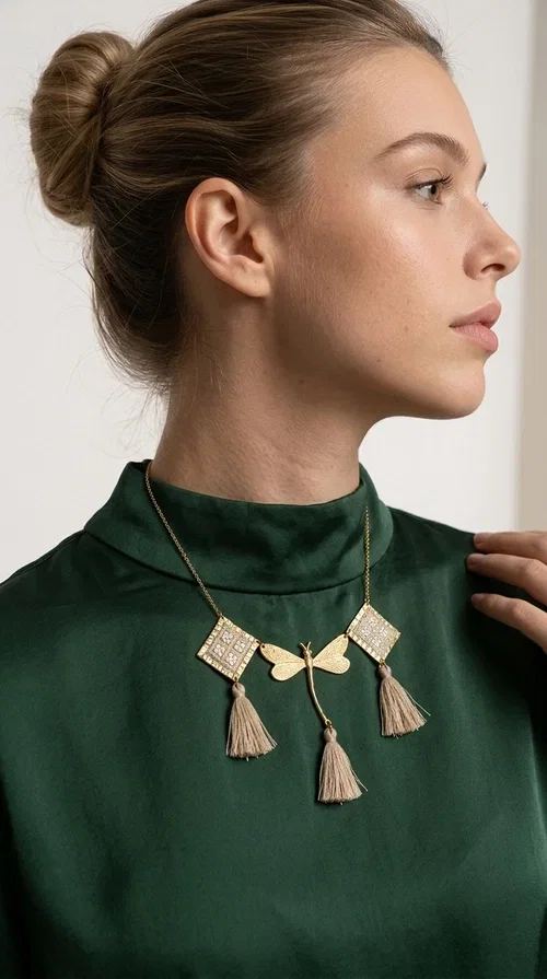 , The statement embroidered ivory necklace with geometric designs is a handmade piece that combines the traditional art of embroidery with a modern aesthetic, creating a result that instantly catches the eye. Designed by Greek Jewelry Designer Aikaterini Chalkiadaki, it is a tribute to folk art and Greek craftsmanship.

The necklace features gold-toned geometric brass elements in a diamond shape, adorned with delicate embroidered motifs in an ivory hue, evoking the rich aesthetic vocabulary of folklore. Among them, a gold metallic dragonfly-shaped element adds grace and movement to the piece. Three fabric tassels in an ivory-beige shade hang elegantly, giving depth and motion to the jewelry.

Ideal for summer outfits, boho and ethnic looks, as well as for elevating a simple dress or blouse. It pairs perfectly with linen clothing, maxi dresses, or casual summer looks.