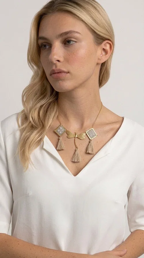 , The statement embroidered ivory necklace with geometric designs is a handmade piece that combines the traditional art of embroidery with a modern aesthetic, creating a result that instantly catches the eye. Designed by Greek Jewelry Designer Aikaterini Chalkiadaki, it is a tribute to folk art and Greek craftsmanship.

The necklace features gold-toned geometric brass elements in a diamond shape, adorned with delicate embroidered motifs in an ivory hue, evoking the rich aesthetic vocabulary of folklore. Among them, a gold metallic dragonfly-shaped element adds grace and movement to the piece. Three fabric tassels in an ivory-beige shade hang elegantly, giving depth and motion to the jewelry.

Ideal for summer outfits, boho and ethnic looks, as well as for elevating a simple dress or blouse. It pairs perfectly with linen clothing, maxi dresses, or casual summer looks.