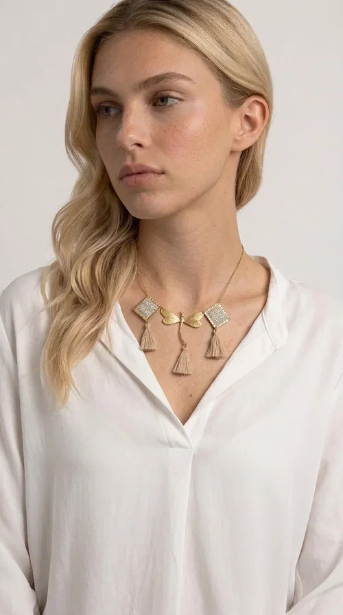 , The statement embroidered ivory necklace with geometric designs is a handmade piece that combines the traditional art of embroidery with a modern aesthetic, creating a result that instantly catches the eye. Designed by Greek Jewelry Designer Aikaterini Chalkiadaki, it is a tribute to folk art and Greek craftsmanship.

The necklace features gold-toned geometric brass elements in a diamond shape, adorned with delicate embroidered motifs in an ivory hue, evoking the rich aesthetic vocabulary of folklore. Among them, a gold metallic dragonfly-shaped element adds grace and movement to the piece. Three fabric tassels in an ivory-beige shade hang elegantly, giving depth and motion to the jewelry.

Ideal for summer outfits, boho and ethnic looks, as well as for elevating a simple dress or blouse. It pairs perfectly with linen clothing, maxi dresses, or casual summer looks.