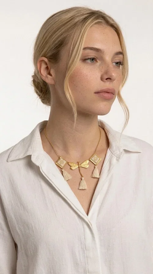 , An embroidered necklace that blends folk aesthetics with modern elegance — the Statement necklace KOL-4771 is the ideal choice for those seeking jewelry with character and warmth.

Designed by Greek Jewelry Designer Aikaterini Chalkiadaki, this necklace is a handmade work of art inspired by Greek folklore aesthetics. Made of brass and fabric, it features geometric embroidered motifs in gold tones alternating with a central butterfly motif, while four ivory fabric tassels add movement and boho-chic flair. The ivory and gold palette creates a timelessly elegant combination, suitable for every season.

Wear it with a white linen shirt or a simple dress to fully showcase its beauty. Ideal for summer looks, weddings, christenings, or even for everyday outings that call for something special.