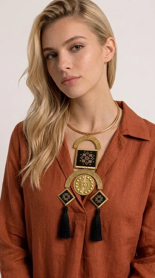 , A statement embroidered necklace that instantly catches the eye — featuring a bold geometric aesthetic, golden details and black tassels that sway gracefully with every step. Designed by Greek Jewelry Designer Aikaterini Chalkiadaki, this handmade necklace blends folklore inspiration with modern sophistication, creating a piece of jewelry that stands out at first glance.

The necklace features a rigid gold-toned brass collar from which geometric elements hang: semicircles, squares and diamond shapes with embroidered patterns on black fabric and gold details. Three black tassels complete the composition, adding movement and depth. The choice of materials — brass and fabric — makes it lightweight despite its impressive size.

Ideal for elevating a simple dress, a monochrome outfit, or even a business casual look. It suits both casual and formal occasions, from everyday wear to evening outings.