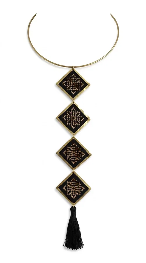 , A statement embroidered necklace that combines tradition with modern aesthetics — ideal for every woman who wants to express herself through her jewelry. Designed by Greek Jewelry Designer Aikaterini Chalkiadaki, this striking long necklace features four diamond-shaped pieces in black fabric with gold-tone geometric embroidered designs, inspired by Greek folk tradition. It is completed with an elegant black tassel at the bottom, while the gold-tone choker base ring adds structure and style.

The necklace is made of brass and fabric, materials that ensure both durability and lightness. The handmade embroidered geometric motifs give each piece a unique character, while the combination of black and gold makes it versatile and timeless. It pairs equally well with casual and formal outfits, instantly offering a bold result.