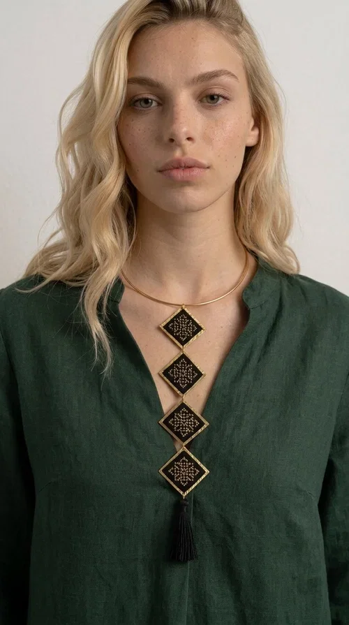 , A statement embroidered necklace that combines tradition with modern aesthetics — ideal for every woman who wants to express herself through her jewelry. Designed by Greek Jewelry Designer Aikaterini Chalkiadaki, this striking long necklace features four diamond-shaped pieces in black fabric with gold-tone geometric embroidered designs, inspired by Greek folk tradition. It is completed with an elegant black tassel at the bottom, while the gold-tone choker base ring adds structure and style.

The necklace is made of brass and fabric, materials that ensure both durability and lightness. The handmade embroidered geometric motifs give each piece a unique character, while the combination of black and gold makes it versatile and timeless. It pairs equally well with casual and formal outfits, instantly offering a bold result.