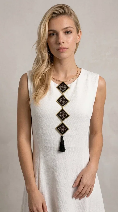 , A statement embroidered necklace that combines tradition with modern aesthetics — ideal for every woman who wants to express herself through her jewelry. Designed by Greek Jewelry Designer Aikaterini Chalkiadaki, this striking long necklace features four diamond-shaped pieces in black fabric with gold-tone geometric embroidered designs, inspired by Greek folk tradition. It is completed with an elegant black tassel at the bottom, while the gold-tone choker base ring adds structure and style.

The necklace is made of brass and fabric, materials that ensure both durability and lightness. The handmade embroidered geometric motifs give each piece a unique character, while the combination of black and gold makes it versatile and timeless. It pairs equally well with casual and formal outfits, instantly offering a bold result.