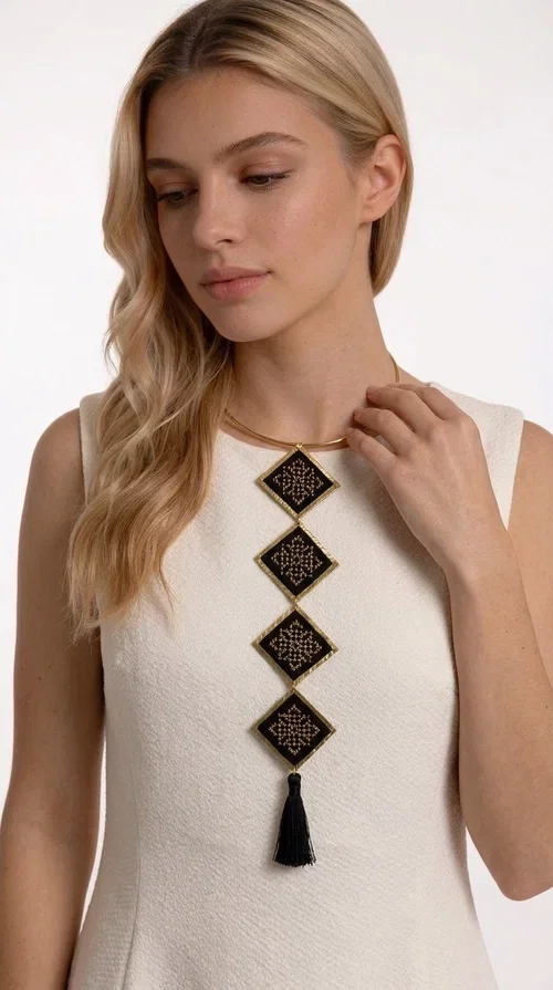 , A statement embroidered necklace that combines tradition with modern aesthetics — ideal for every woman who wants to express herself through her jewelry. Designed by Greek Jewelry Designer Aikaterini Chalkiadaki, this striking long necklace features four diamond-shaped pieces in black fabric with gold-tone geometric embroidered designs, inspired by Greek folk tradition. It is completed with an elegant black tassel at the bottom, while the gold-tone choker base ring adds structure and style.

The necklace is made of brass and fabric, materials that ensure both durability and lightness. The handmade embroidered geometric motifs give each piece a unique character, while the combination of black and gold makes it versatile and timeless. It pairs equally well with casual and formal outfits, instantly offering a bold result.