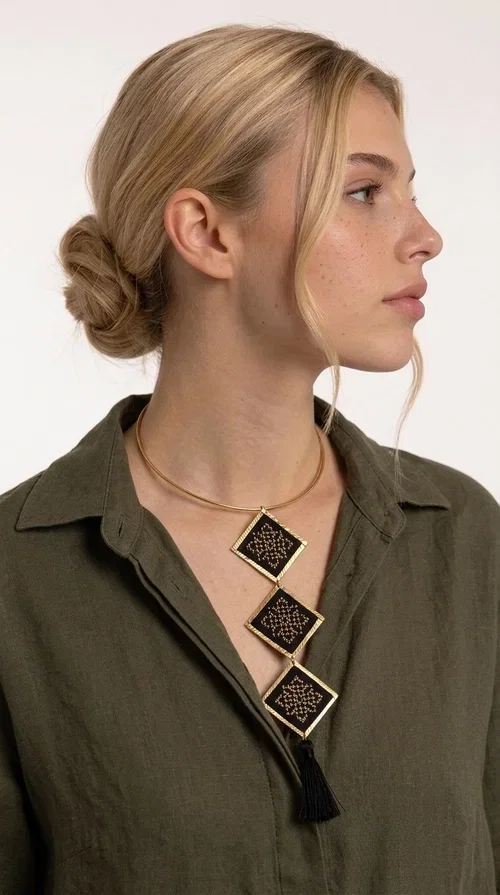 , A statement embroidered necklace that combines tradition with modern aesthetics — ideal for every woman who wants to express herself through her jewelry. Designed by Greek Jewelry Designer Aikaterini Chalkiadaki, this striking long necklace features four diamond-shaped pieces in black fabric with gold-tone geometric embroidered designs, inspired by Greek folk tradition. It is completed with an elegant black tassel at the bottom, while the gold-tone choker base ring adds structure and style.

The necklace is made of brass and fabric, materials that ensure both durability and lightness. The handmade embroidered geometric motifs give each piece a unique character, while the combination of black and gold makes it versatile and timeless. It pairs equally well with casual and formal outfits, instantly offering a bold result.