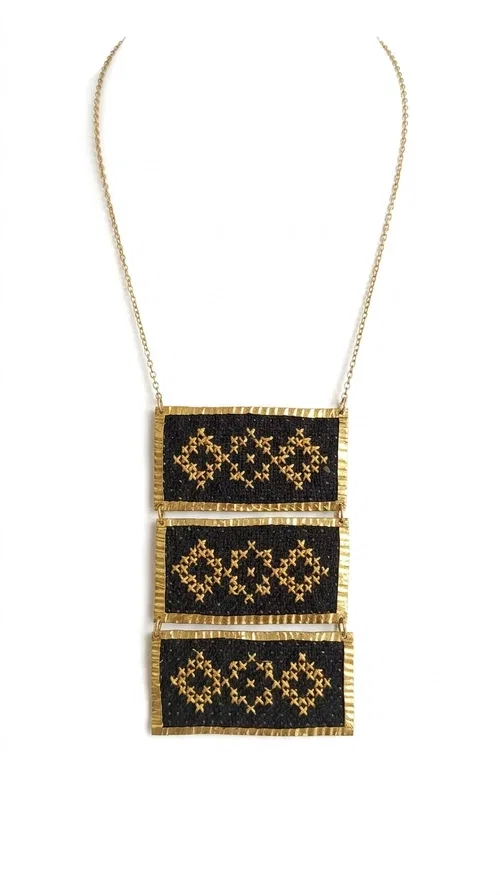 , An embroidered necklace that combines traditional Greek aesthetics with modern fashion — the Statement necklace KOL-4774 is a handmade creation that instantly catches the eye.

Designed by Greek Jewelry Designer Aikaterini Chalkiadaki, this necklace features three rectangular fabric plaques in deep black, adorned with gold-toned embroidered geometric designs inspired by Greek folk tradition. The frame of each plaque, made of gold-toned brass, gives the piece a rich, striking presence. The accompanying brass chain keeps the composition light on the neck, while the overall look exudes a unique blend of ethnic and contemporary style.

Ideal for women who love statement jewelry and want to elevate simple outfits — a linen shirt, a black dress, or even a casual look — with a wonderful touch of individuality. Perfect for nights out, events, weddings, or everyday wear when you want to stand out.