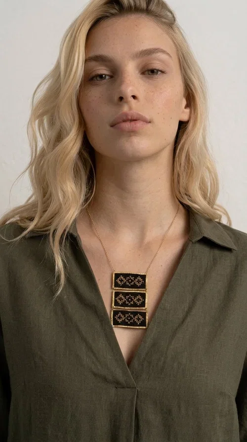 , An embroidered necklace that combines traditional Greek aesthetics with modern fashion — the Statement necklace KOL-4774 is a handmade creation that instantly catches the eye.

Designed by Greek Jewelry Designer Aikaterini Chalkiadaki, this necklace features three rectangular fabric plaques in deep black, adorned with gold-toned embroidered geometric designs inspired by Greek folk tradition. The frame of each plaque, made of gold-toned brass, gives the piece a rich, striking presence. The accompanying brass chain keeps the composition light on the neck, while the overall look exudes a unique blend of ethnic and contemporary style.

Ideal for women who love statement jewelry and want to elevate simple outfits — a linen shirt, a black dress, or even a casual look — with a wonderful touch of individuality. Perfect for nights out, events, weddings, or everyday wear when you want to stand out.
