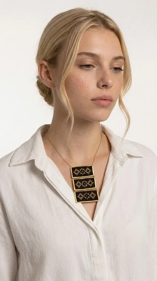 , An embroidered necklace that combines traditional Greek aesthetics with modern fashion — the Statement necklace KOL-4774 is a handmade creation that instantly catches the eye.

Designed by Greek Jewelry Designer Aikaterini Chalkiadaki, this necklace features three rectangular fabric plaques in deep black, adorned with gold-toned embroidered geometric designs inspired by Greek folk tradition. The frame of each plaque, made of gold-toned brass, gives the piece a rich, striking presence. The accompanying brass chain keeps the composition light on the neck, while the overall look exudes a unique blend of ethnic and contemporary style.

Ideal for women who love statement jewelry and want to elevate simple outfits — a linen shirt, a black dress, or even a casual look — with a wonderful touch of individuality. Perfect for nights out, events, weddings, or everyday wear when you want to stand out.