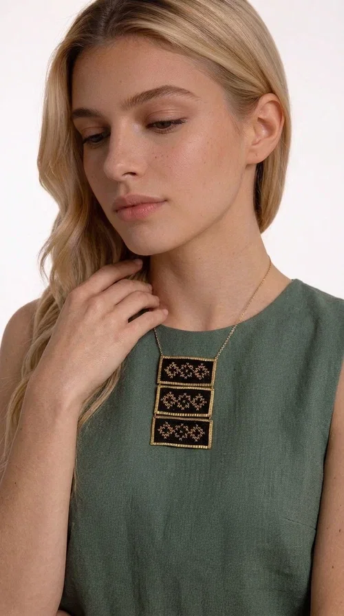 , An embroidered necklace that combines traditional Greek aesthetics with modern fashion — the Statement necklace KOL-4774 is a handmade creation that instantly catches the eye.

Designed by Greek Jewelry Designer Aikaterini Chalkiadaki, this necklace features three rectangular fabric plaques in deep black, adorned with gold-toned embroidered geometric designs inspired by Greek folk tradition. The frame of each plaque, made of gold-toned brass, gives the piece a rich, striking presence. The accompanying brass chain keeps the composition light on the neck, while the overall look exudes a unique blend of ethnic and contemporary style.

Ideal for women who love statement jewelry and want to elevate simple outfits — a linen shirt, a black dress, or even a casual look — with a wonderful touch of individuality. Perfect for nights out, events, weddings, or everyday wear when you want to stand out.