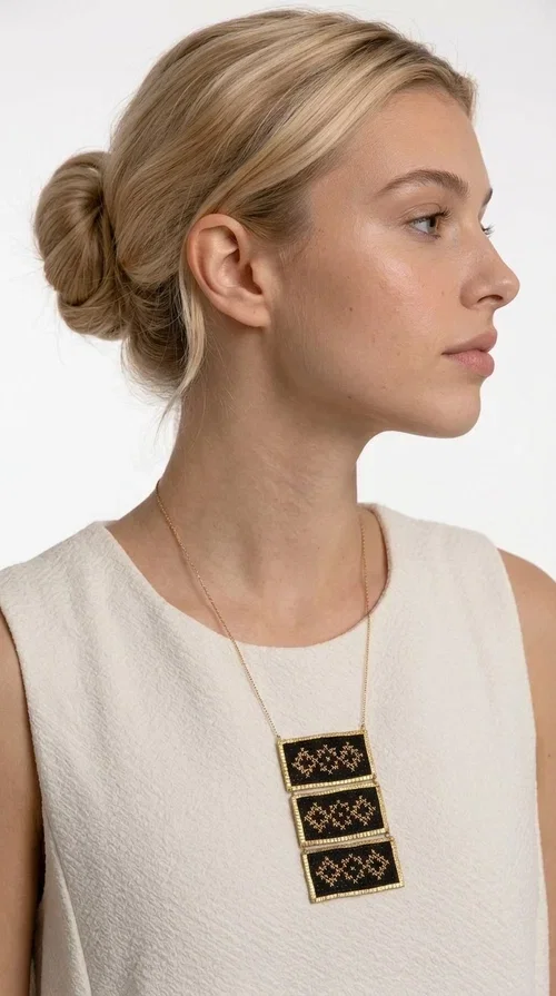 , An embroidered necklace that combines traditional Greek aesthetics with modern fashion — the Statement necklace KOL-4774 is a handmade creation that instantly catches the eye.

Designed by Greek Jewelry Designer Aikaterini Chalkiadaki, this necklace features three rectangular fabric plaques in deep black, adorned with gold-toned embroidered geometric designs inspired by Greek folk tradition. The frame of each plaque, made of gold-toned brass, gives the piece a rich, striking presence. The accompanying brass chain keeps the composition light on the neck, while the overall look exudes a unique blend of ethnic and contemporary style.

Ideal for women who love statement jewelry and want to elevate simple outfits — a linen shirt, a black dress, or even a casual look — with a wonderful touch of individuality. Perfect for nights out, events, weddings, or everyday wear when you want to stand out.