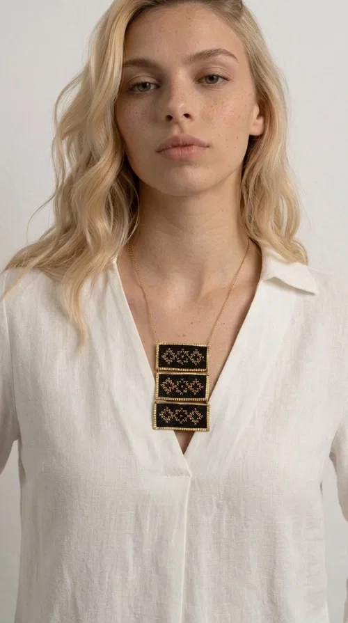 , An embroidered necklace that combines traditional Greek aesthetics with modern fashion — the Statement necklace KOL-4774 is a handmade creation that instantly catches the eye.

Designed by Greek Jewelry Designer Aikaterini Chalkiadaki, this necklace features three rectangular fabric plaques in deep black, adorned with gold-toned embroidered geometric designs inspired by Greek folk tradition. The frame of each plaque, made of gold-toned brass, gives the piece a rich, striking presence. The accompanying brass chain keeps the composition light on the neck, while the overall look exudes a unique blend of ethnic and contemporary style.

Ideal for women who love statement jewelry and want to elevate simple outfits — a linen shirt, a black dress, or even a casual look — with a wonderful touch of individuality. Perfect for nights out, events, weddings, or everyday wear when you want to stand out.