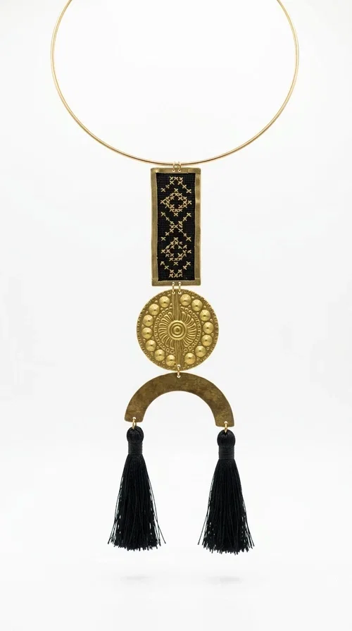 , The statement embroidered necklace with geometric patterns in black is a jewel that never goes unnoticed — bold, handmade, and full of character. Designed by Greek Jewelry Designer Aikaterini Chalkiadaki, it combines the traditional art of embroidery with a modern aesthetic, creating a piece with strong personality and Greek soul.

The design features a gold-tone brass torque collar, from which hangs a rectangular embroidered panel with black geometric motifs inspired by Greek folk tradition. This is followed by a striking embossed brass disc with a sun motif, and at the bottom, a semicircular element adorned with three black tassels, adding movement and femininity to the overall look.

Ideal for looks you want to stand out in — from casual outfits with a linen dress or a plain t-shirt to evening appearances. Black and gold blend harmoniously with almost any clothing color.