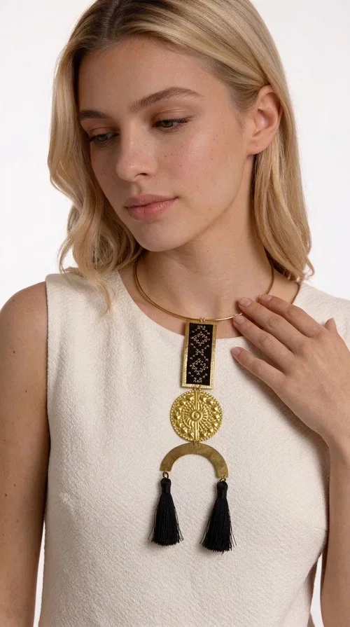 , The statement embroidered necklace with geometric patterns in black is a jewel that never goes unnoticed — bold, handmade, and full of character. Designed by Greek Jewelry Designer Aikaterini Chalkiadaki, it combines the traditional art of embroidery with a modern aesthetic, creating a piece with strong personality and Greek soul.

The design features a gold-tone brass torque collar, from which hangs a rectangular embroidered panel with black geometric motifs inspired by Greek folk tradition. This is followed by a striking embossed brass disc with a sun motif, and at the bottom, a semicircular element adorned with three black tassels, adding movement and femininity to the overall look.

Ideal for looks you want to stand out in — from casual outfits with a linen dress or a plain t-shirt to evening appearances. Black and gold blend harmoniously with almost any clothing color.