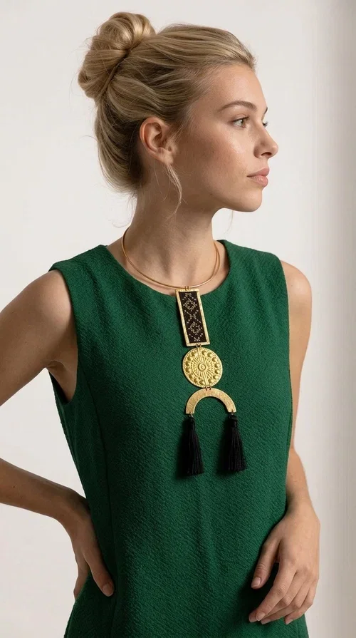 , The statement embroidered necklace with geometric patterns in black is a jewel that never goes unnoticed — bold, handmade, and full of character. Designed by Greek Jewelry Designer Aikaterini Chalkiadaki, it combines the traditional art of embroidery with a modern aesthetic, creating a piece with strong personality and Greek soul.

The design features a gold-tone brass torque collar, from which hangs a rectangular embroidered panel with black geometric motifs inspired by Greek folk tradition. This is followed by a striking embossed brass disc with a sun motif, and at the bottom, a semicircular element adorned with three black tassels, adding movement and femininity to the overall look.

Ideal for looks you want to stand out in — from casual outfits with a linen dress or a plain t-shirt to evening appearances. Black and gold blend harmoniously with almost any clothing color.