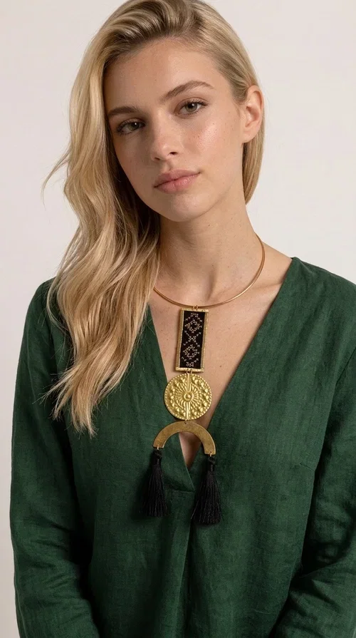 , The statement embroidered necklace with geometric patterns in black is a jewel that never goes unnoticed — bold, handmade, and full of character. Designed by Greek Jewelry Designer Aikaterini Chalkiadaki, it combines the traditional art of embroidery with a modern aesthetic, creating a piece with strong personality and Greek soul.

The design features a gold-tone brass torque collar, from which hangs a rectangular embroidered panel with black geometric motifs inspired by Greek folk tradition. This is followed by a striking embossed brass disc with a sun motif, and at the bottom, a semicircular element adorned with three black tassels, adding movement and femininity to the overall look.

Ideal for looks you want to stand out in — from casual outfits with a linen dress or a plain t-shirt to evening appearances. Black and gold blend harmoniously with almost any clothing color.
