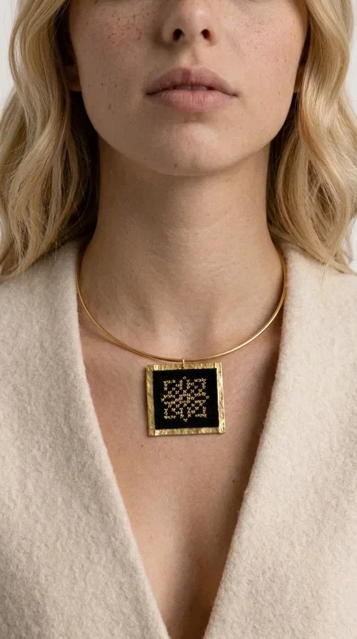 , An embroidered necklace that instantly catches every eye — this Statement Necklace with geometric patterns on a black background blends the traditional art of embroidery with a modern, minimal aesthetic.

Designed by Greek Jewelry Designer Aikaterini Chalkiadaki, this handmade necklace is a unique piece that showcases Greek craftsmanship in all its glory. The square pendant, made of brass and fabric, features an intricately worked geometric motif inspired by traditional folk art — creating an effect that resembles embroidery in a black-and-gold color palette. The choker hugs the neck with elegance, while the raised gold frame of the pendant adds a distinctive depth and character to the overall look.

Ideal for casual style with a blazer or for evening looks, this striking necklace pairs equally well with a white shirt or a black dress. If you're looking for large, eye-catching necklaces with soul and story, this is the answer.
