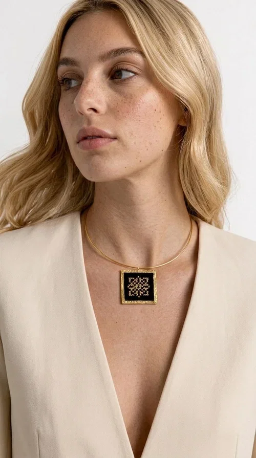 , An embroidered necklace that instantly catches every eye — this Statement Necklace with geometric patterns on a black background blends the traditional art of embroidery with a modern, minimal aesthetic.

Designed by Greek Jewelry Designer Aikaterini Chalkiadaki, this handmade necklace is a unique piece that showcases Greek craftsmanship in all its glory. The square pendant, made of brass and fabric, features an intricately worked geometric motif inspired by traditional folk art — creating an effect that resembles embroidery in a black-and-gold color palette. The choker hugs the neck with elegance, while the raised gold frame of the pendant adds a distinctive depth and character to the overall look.

Ideal for casual style with a blazer or for evening looks, this striking necklace pairs equally well with a white shirt or a black dress. If you're looking for large, eye-catching necklaces with soul and story, this is the answer.
