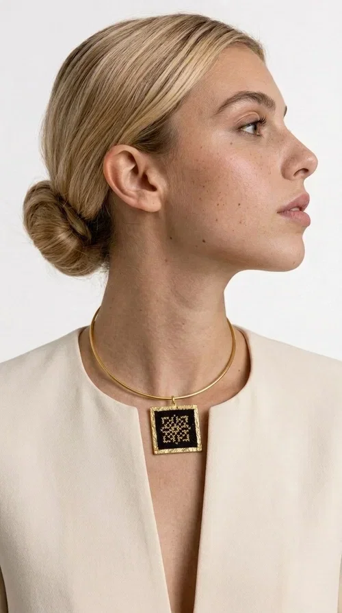 , An embroidered necklace that instantly catches every eye — this Statement Necklace with geometric patterns on a black background blends the traditional art of embroidery with a modern, minimal aesthetic.

Designed by Greek Jewelry Designer Aikaterini Chalkiadaki, this handmade necklace is a unique piece that showcases Greek craftsmanship in all its glory. The square pendant, made of brass and fabric, features an intricately worked geometric motif inspired by traditional folk art — creating an effect that resembles embroidery in a black-and-gold color palette. The choker hugs the neck with elegance, while the raised gold frame of the pendant adds a distinctive depth and character to the overall look.

Ideal for casual style with a blazer or for evening looks, this striking necklace pairs equally well with a white shirt or a black dress. If you're looking for large, eye-catching necklaces with soul and story, this is the answer.