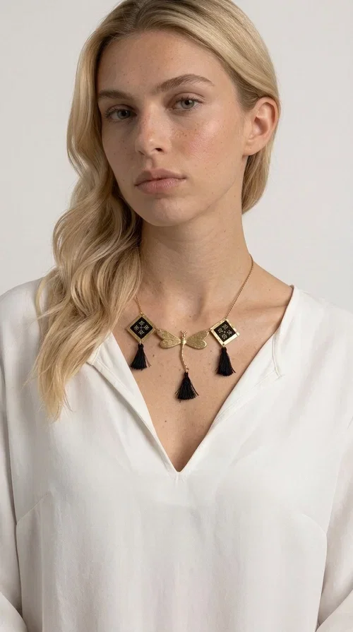 , A statement embroidered necklace that instantly catches the eye — the perfect piece for every woman who wants to express herself with style and personality. Designed by Greek Jewelry Designer Aikaterini Chalkiadaki, this unique necklace combines the traditional art of embroidery with a modern, striking result. Its geometric composition and bold black palette make it a timeless statement piece that truly stands out.

The necklace features three square brass motifs with black embroidered geometric patterns, inspired by folk aesthetics. At the center sits a striking gold-tone metal element shaped like a dragonfly or butterfly, while elegant black fabric tassels hang from each motif, adding movement and lightness. The chain is gold-toned brass, durable and lightweight to wear.

Ideal for daytime looks with white or monochrome outfits, as well as for evening occasions that call for character. It pairs perfectly with simple dresses, tailored outfits, and casual looks.