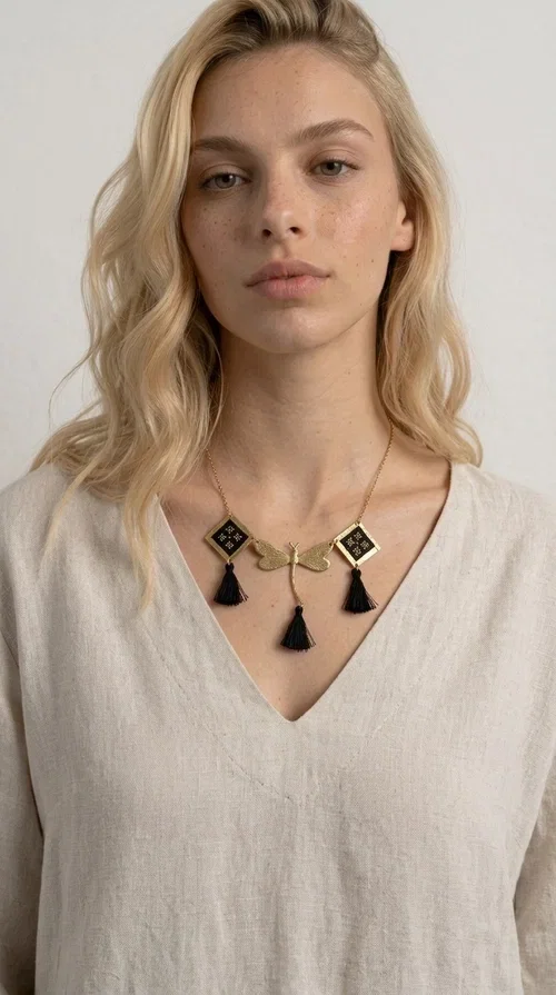 , A statement embroidered necklace that instantly catches the eye — the perfect piece for every woman who wants to express herself with style and personality. Designed by Greek Jewelry Designer Aikaterini Chalkiadaki, this unique necklace combines the traditional art of embroidery with a modern, striking result. Its geometric composition and bold black palette make it a timeless statement piece that truly stands out.

The necklace features three square brass motifs with black embroidered geometric patterns, inspired by folk aesthetics. At the center sits a striking gold-tone metal element shaped like a dragonfly or butterfly, while elegant black fabric tassels hang from each motif, adding movement and lightness. The chain is gold-toned brass, durable and lightweight to wear.

Ideal for daytime looks with white or monochrome outfits, as well as for evening occasions that call for character. It pairs perfectly with simple dresses, tailored outfits, and casual looks.