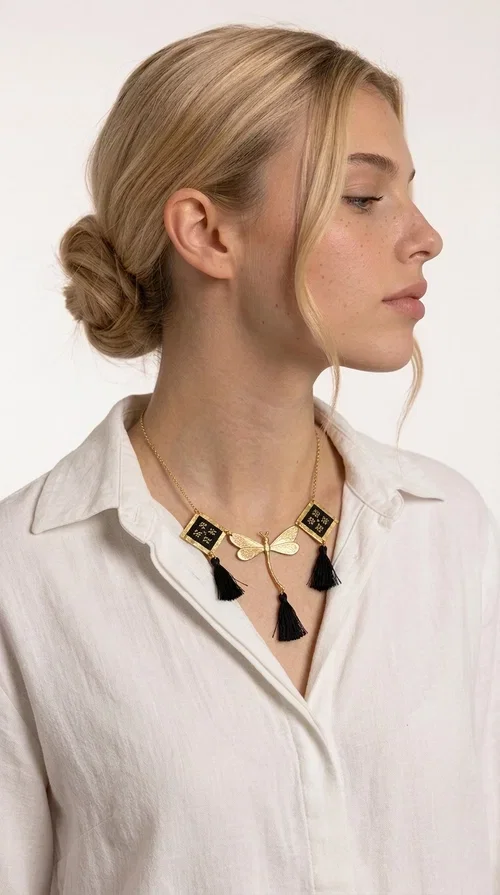 , A statement embroidered necklace that instantly catches the eye — the perfect piece for every woman who wants to express herself with style and personality. Designed by Greek Jewelry Designer Aikaterini Chalkiadaki, this unique necklace combines the traditional art of embroidery with a modern, striking result. Its geometric composition and bold black palette make it a timeless statement piece that truly stands out.

The necklace features three square brass motifs with black embroidered geometric patterns, inspired by folk aesthetics. At the center sits a striking gold-tone metal element shaped like a dragonfly or butterfly, while elegant black fabric tassels hang from each motif, adding movement and lightness. The chain is gold-toned brass, durable and lightweight to wear.

Ideal for daytime looks with white or monochrome outfits, as well as for evening occasions that call for character. It pairs perfectly with simple dresses, tailored outfits, and casual looks.