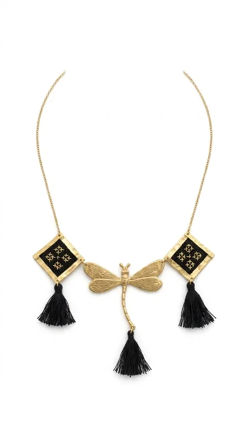 , A statement embroidered necklace that instantly catches the eye — the perfect piece for every woman who wants to express herself with style and personality. Designed by Greek Jewelry Designer Aikaterini Chalkiadaki, this unique necklace combines the traditional art of embroidery with a modern, striking result. Its geometric composition and bold black palette make it a timeless statement piece that truly stands out.

The necklace features three square brass motifs with black embroidered geometric patterns, inspired by folk aesthetics. At the center sits a striking gold-tone metal element shaped like a dragonfly or butterfly, while elegant black fabric tassels hang from each motif, adding movement and lightness. The chain is gold-toned brass, durable and lightweight to wear.

Ideal for daytime looks with white or monochrome outfits, as well as for evening occasions that call for character. It pairs perfectly with simple dresses, tailored outfits, and casual looks.