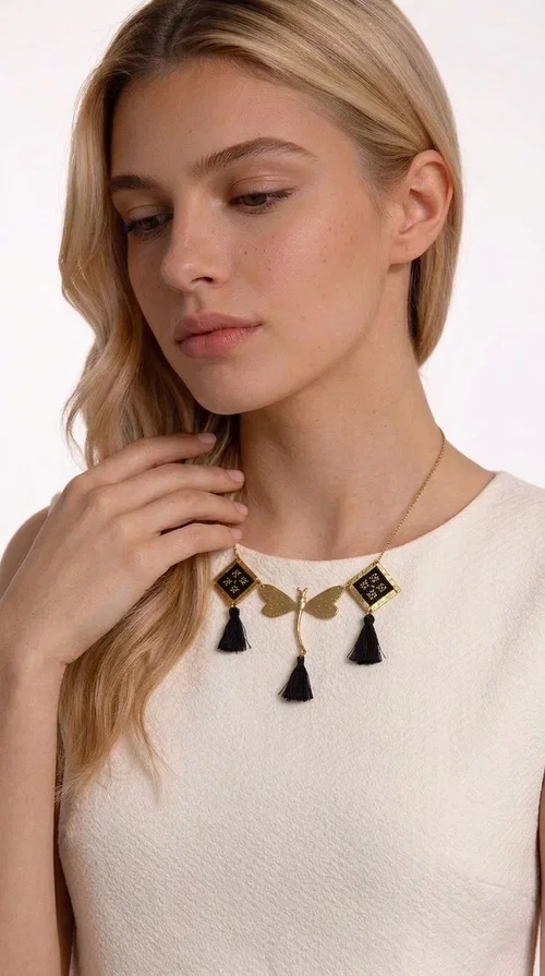 , A statement embroidered necklace that instantly catches the eye — the perfect piece for every woman who wants to express herself with style and personality. Designed by Greek Jewelry Designer Aikaterini Chalkiadaki, this unique necklace combines the traditional art of embroidery with a modern, striking result. Its geometric composition and bold black palette make it a timeless statement piece that truly stands out.

The necklace features three square brass motifs with black embroidered geometric patterns, inspired by folk aesthetics. At the center sits a striking gold-tone metal element shaped like a dragonfly or butterfly, while elegant black fabric tassels hang from each motif, adding movement and lightness. The chain is gold-toned brass, durable and lightweight to wear.

Ideal for daytime looks with white or monochrome outfits, as well as for evening occasions that call for character. It pairs perfectly with simple dresses, tailored outfits, and casual looks.