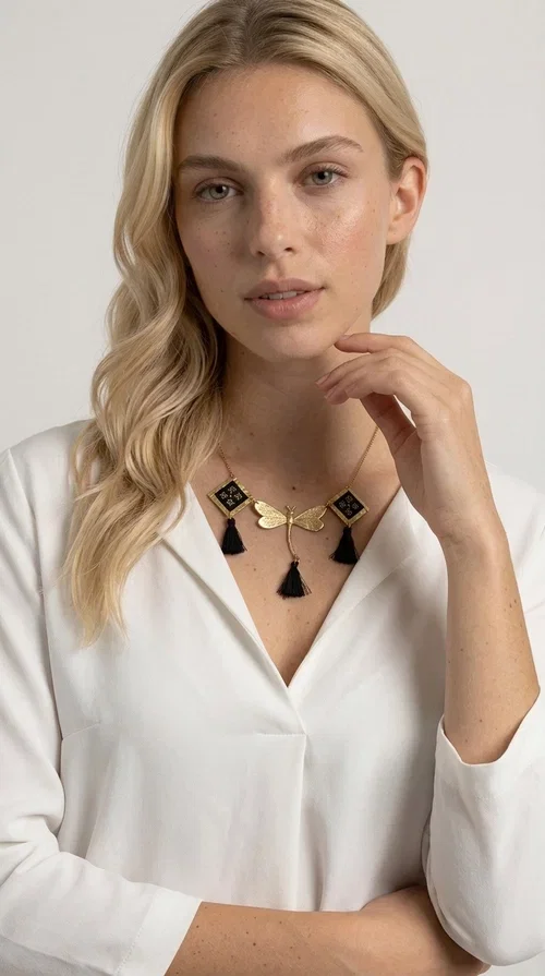 , A statement embroidered necklace that instantly catches the eye — the perfect piece for every woman who wants to express herself with style and personality. Designed by Greek Jewelry Designer Aikaterini Chalkiadaki, this unique necklace combines the traditional art of embroidery with a modern, striking result. Its geometric composition and bold black palette make it a timeless statement piece that truly stands out.

The necklace features three square brass motifs with black embroidered geometric patterns, inspired by folk aesthetics. At the center sits a striking gold-tone metal element shaped like a dragonfly or butterfly, while elegant black fabric tassels hang from each motif, adding movement and lightness. The chain is gold-toned brass, durable and lightweight to wear.

Ideal for daytime looks with white or monochrome outfits, as well as for evening occasions that call for character. It pairs perfectly with simple dresses, tailored outfits, and casual looks.