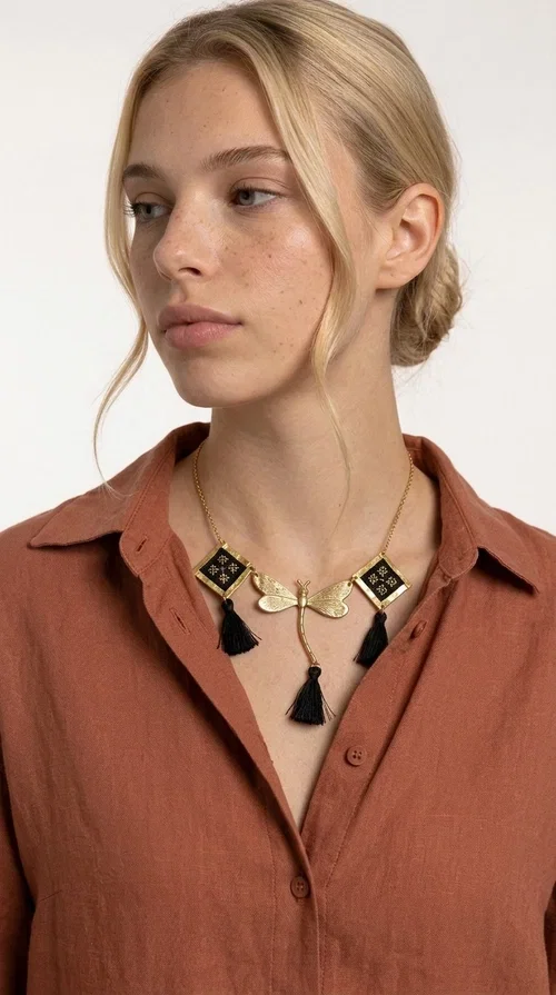 , A statement embroidered necklace that instantly catches the eye — the perfect piece for every woman who wants to express herself with style and personality. Designed by Greek Jewelry Designer Aikaterini Chalkiadaki, this unique necklace combines the traditional art of embroidery with a modern, striking result. Its geometric composition and bold black palette make it a timeless statement piece that truly stands out.

The necklace features three square brass motifs with black embroidered geometric patterns, inspired by folk aesthetics. At the center sits a striking gold-tone metal element shaped like a dragonfly or butterfly, while elegant black fabric tassels hang from each motif, adding movement and lightness. The chain is gold-toned brass, durable and lightweight to wear.

Ideal for daytime looks with white or monochrome outfits, as well as for evening occasions that call for character. It pairs perfectly with simple dresses, tailored outfits, and casual looks.