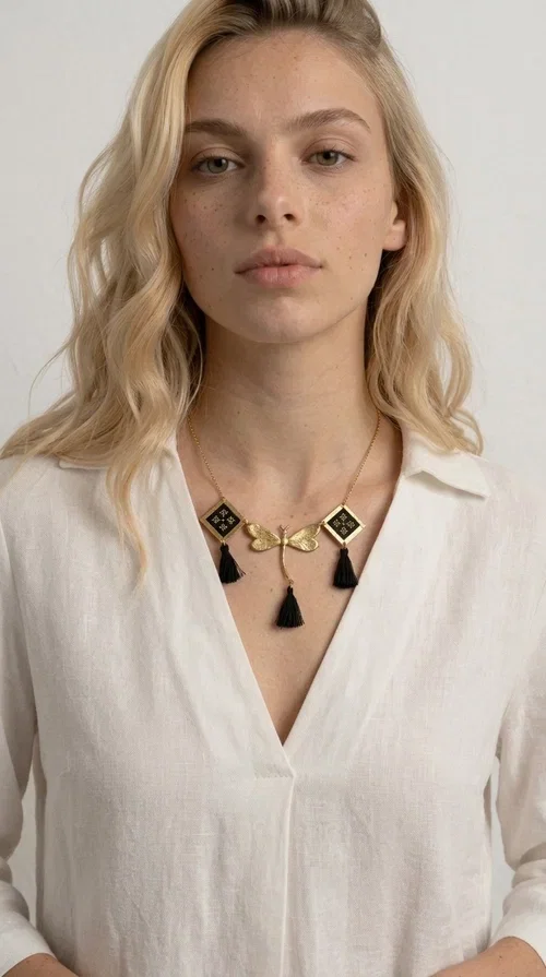 , A statement embroidered necklace that instantly catches the eye — the perfect piece for every woman who wants to express herself with style and personality. Designed by Greek Jewelry Designer Aikaterini Chalkiadaki, this unique necklace combines the traditional art of embroidery with a modern, striking result. Its geometric composition and bold black palette make it a timeless statement piece that truly stands out.

The necklace features three square brass motifs with black embroidered geometric patterns, inspired by folk aesthetics. At the center sits a striking gold-tone metal element shaped like a dragonfly or butterfly, while elegant black fabric tassels hang from each motif, adding movement and lightness. The chain is gold-toned brass, durable and lightweight to wear.

Ideal for daytime looks with white or monochrome outfits, as well as for evening occasions that call for character. It pairs perfectly with simple dresses, tailored outfits, and casual looks.