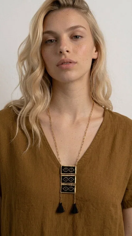 , An embroidered necklace that blends tradition with contemporary style — the Statement Necklace KOL-4754 is the perfect choice for any woman who wants to express herself through her jewelry. Designed by Greek Jewelry Designer Aikaterini Chalkiadaki, this handmade necklace features geometric embroidered patterns inspired by Greek folk tradition, creating a unique piece full of character.

Three rectangular brass frames in a gold hue are adorned with black embroidery in geometric motifs, while black tassels at the bottom add movement and dramatic flair. The gold paperclip-style chain completes the look with an elegant, modern touch. The result is a striking long necklace that suits both everyday and evening outfits equally well.

Wear it over a simple shirt or dress to create a look full of personality. It's the perfect gift choice, and also the perfect way to turn heads at an evening event.