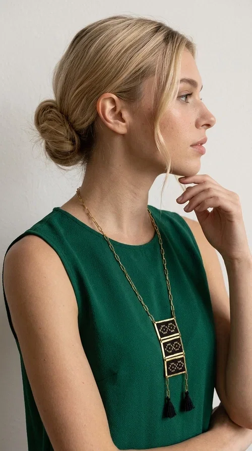 , An embroidered necklace that blends tradition with contemporary style — the Statement Necklace KOL-4754 is the perfect choice for any woman who wants to express herself through her jewelry. Designed by Greek Jewelry Designer Aikaterini Chalkiadaki, this handmade necklace features geometric embroidered patterns inspired by Greek folk tradition, creating a unique piece full of character.

Three rectangular brass frames in a gold hue are adorned with black embroidery in geometric motifs, while black tassels at the bottom add movement and dramatic flair. The gold paperclip-style chain completes the look with an elegant, modern touch. The result is a striking long necklace that suits both everyday and evening outfits equally well.

Wear it over a simple shirt or dress to create a look full of personality. It's the perfect gift choice, and also the perfect way to turn heads at an evening event.
