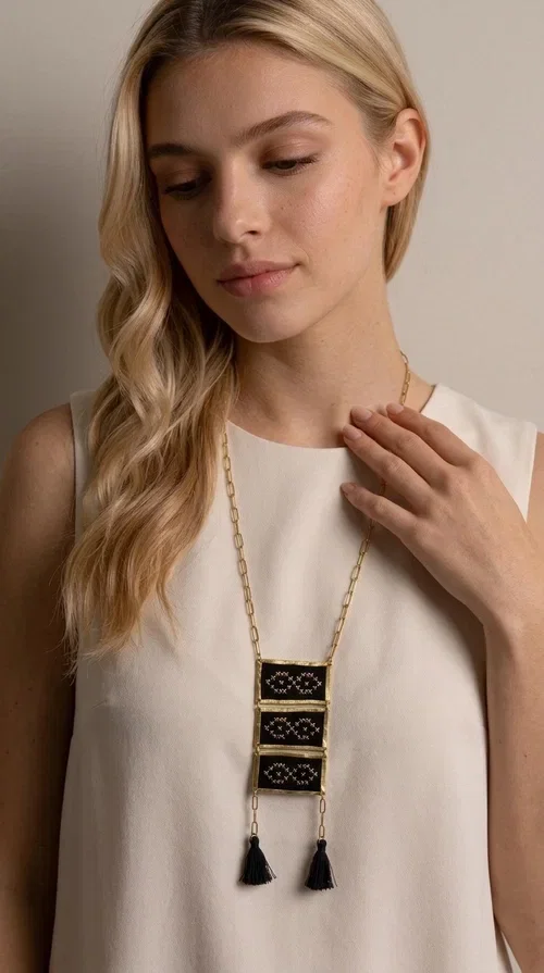 , An embroidered necklace that blends tradition with contemporary style — the Statement Necklace KOL-4754 is the perfect choice for any woman who wants to express herself through her jewelry. Designed by Greek Jewelry Designer Aikaterini Chalkiadaki, this handmade necklace features geometric embroidered patterns inspired by Greek folk tradition, creating a unique piece full of character.

Three rectangular brass frames in a gold hue are adorned with black embroidery in geometric motifs, while black tassels at the bottom add movement and dramatic flair. The gold paperclip-style chain completes the look with an elegant, modern touch. The result is a striking long necklace that suits both everyday and evening outfits equally well.

Wear it over a simple shirt or dress to create a look full of personality. It's the perfect gift choice, and also the perfect way to turn heads at an evening event.