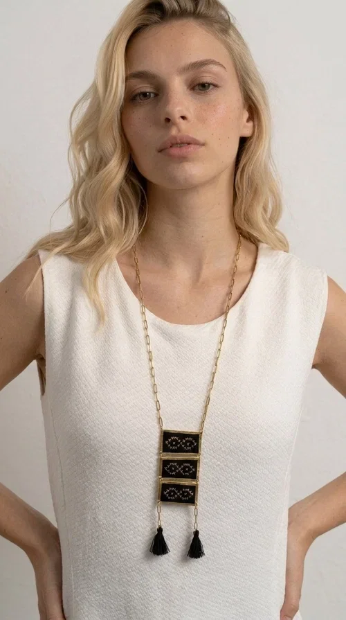 , An embroidered necklace that blends tradition with contemporary style — the Statement Necklace KOL-4754 is the perfect choice for any woman who wants to express herself through her jewelry. Designed by Greek Jewelry Designer Aikaterini Chalkiadaki, this handmade necklace features geometric embroidered patterns inspired by Greek folk tradition, creating a unique piece full of character.

Three rectangular brass frames in a gold hue are adorned with black embroidery in geometric motifs, while black tassels at the bottom add movement and dramatic flair. The gold paperclip-style chain completes the look with an elegant, modern touch. The result is a striking long necklace that suits both everyday and evening outfits equally well.

Wear it over a simple shirt or dress to create a look full of personality. It's the perfect gift choice, and also the perfect way to turn heads at an evening event.