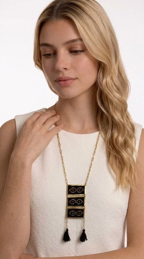 , An embroidered necklace that blends tradition with contemporary style — the Statement Necklace KOL-4754 is the perfect choice for any woman who wants to express herself through her jewelry. Designed by Greek Jewelry Designer Aikaterini Chalkiadaki, this handmade necklace features geometric embroidered patterns inspired by Greek folk tradition, creating a unique piece full of character.

Three rectangular brass frames in a gold hue are adorned with black embroidery in geometric motifs, while black tassels at the bottom add movement and dramatic flair. The gold paperclip-style chain completes the look with an elegant, modern touch. The result is a striking long necklace that suits both everyday and evening outfits equally well.

Wear it over a simple shirt or dress to create a look full of personality. It's the perfect gift choice, and also the perfect way to turn heads at an evening event.