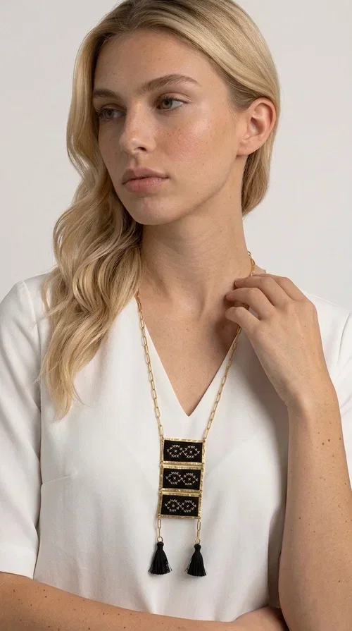 , An embroidered necklace that blends tradition with contemporary style — the Statement Necklace KOL-4754 is the perfect choice for any woman who wants to express herself through her jewelry. Designed by Greek Jewelry Designer Aikaterini Chalkiadaki, this handmade necklace features geometric embroidered patterns inspired by Greek folk tradition, creating a unique piece full of character.

Three rectangular brass frames in a gold hue are adorned with black embroidery in geometric motifs, while black tassels at the bottom add movement and dramatic flair. The gold paperclip-style chain completes the look with an elegant, modern touch. The result is a striking long necklace that suits both everyday and evening outfits equally well.

Wear it over a simple shirt or dress to create a look full of personality. It's the perfect gift choice, and also the perfect way to turn heads at an evening event.