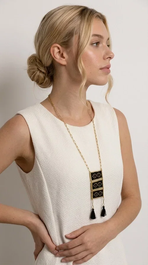 , An embroidered necklace that blends tradition with contemporary style — the Statement Necklace KOL-4754 is the perfect choice for any woman who wants to express herself through her jewelry. Designed by Greek Jewelry Designer Aikaterini Chalkiadaki, this handmade necklace features geometric embroidered patterns inspired by Greek folk tradition, creating a unique piece full of character.

Three rectangular brass frames in a gold hue are adorned with black embroidery in geometric motifs, while black tassels at the bottom add movement and dramatic flair. The gold paperclip-style chain completes the look with an elegant, modern touch. The result is a striking long necklace that suits both everyday and evening outfits equally well.

Wear it over a simple shirt or dress to create a look full of personality. It's the perfect gift choice, and also the perfect way to turn heads at an evening event.