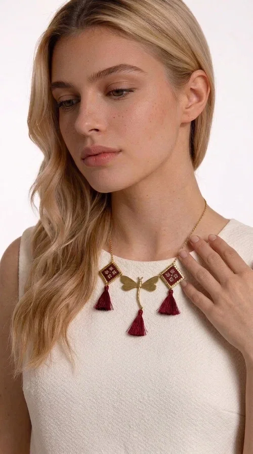 , The statement embroidered burgundy necklace is a jewel that instantly draws attention — featuring geometric patterns inspired by Greek folk art and a color palette that expresses richness and character. Designed by Greek Jewelry Designer Aikaterini Chalkiadaki, this handmade necklace combines gold-tone brass with embroidered fabric elements in deep burgundy, creating a result that balances between folk and contemporary style.

The necklace features two diamond-shaped pieces with embroidered geometric motifs, a central brass beetle-shaped link, and three burgundy tassels that add movement and drama to the overall look. The gold-tone brass chain completes the composition in an elegant, minimal way that lets the main elements shine. It is ideal as a statement piece for everyday looks as well as for evening occasions.

Wear it with a simple solid-colored shirt or dress to highlight its rich detail. It pairs exceptionally well with earthy tones, greens, and blacks.