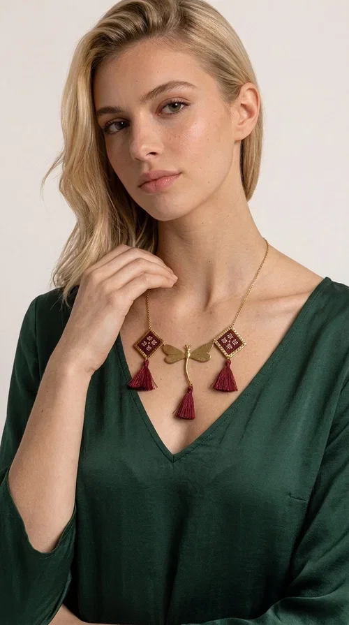 , The statement embroidered burgundy necklace is a jewel that instantly draws attention — featuring geometric patterns inspired by Greek folk art and a color palette that expresses richness and character. Designed by Greek Jewelry Designer Aikaterini Chalkiadaki, this handmade necklace combines gold-tone brass with embroidered fabric elements in deep burgundy, creating a result that balances between folk and contemporary style.

The necklace features two diamond-shaped pieces with embroidered geometric motifs, a central brass beetle-shaped link, and three burgundy tassels that add movement and drama to the overall look. The gold-tone brass chain completes the composition in an elegant, minimal way that lets the main elements shine. It is ideal as a statement piece for everyday looks as well as for evening occasions.

Wear it with a simple solid-colored shirt or dress to highlight its rich detail. It pairs exceptionally well with earthy tones, greens, and blacks.
