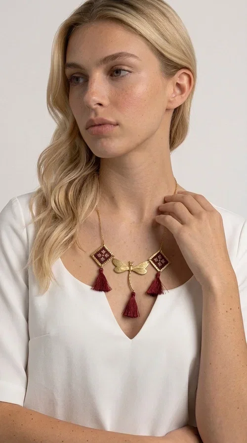 , The statement embroidered burgundy necklace is a jewel that instantly draws attention — featuring geometric patterns inspired by Greek folk art and a color palette that expresses richness and character. Designed by Greek Jewelry Designer Aikaterini Chalkiadaki, this handmade necklace combines gold-tone brass with embroidered fabric elements in deep burgundy, creating a result that balances between folk and contemporary style.

The necklace features two diamond-shaped pieces with embroidered geometric motifs, a central brass beetle-shaped link, and three burgundy tassels that add movement and drama to the overall look. The gold-tone brass chain completes the composition in an elegant, minimal way that lets the main elements shine. It is ideal as a statement piece for everyday looks as well as for evening occasions.

Wear it with a simple solid-colored shirt or dress to highlight its rich detail. It pairs exceptionally well with earthy tones, greens, and blacks.