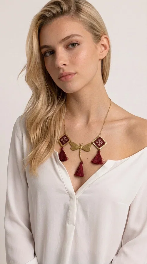 , The statement embroidered burgundy necklace is a jewel that instantly draws attention — featuring geometric patterns inspired by Greek folk art and a color palette that expresses richness and character. Designed by Greek Jewelry Designer Aikaterini Chalkiadaki, this handmade necklace combines gold-tone brass with embroidered fabric elements in deep burgundy, creating a result that balances between folk and contemporary style.

The necklace features two diamond-shaped pieces with embroidered geometric motifs, a central brass beetle-shaped link, and three burgundy tassels that add movement and drama to the overall look. The gold-tone brass chain completes the composition in an elegant, minimal way that lets the main elements shine. It is ideal as a statement piece for everyday looks as well as for evening occasions.

Wear it with a simple solid-colored shirt or dress to highlight its rich detail. It pairs exceptionally well with earthy tones, greens, and blacks.