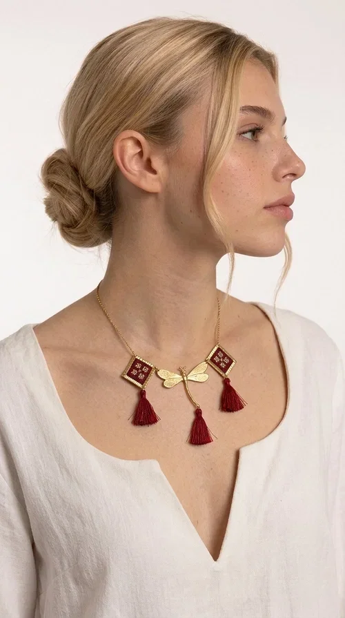 , The statement embroidered burgundy necklace is a jewel that instantly draws attention — featuring geometric patterns inspired by Greek folk art and a color palette that expresses richness and character. Designed by Greek Jewelry Designer Aikaterini Chalkiadaki, this handmade necklace combines gold-tone brass with embroidered fabric elements in deep burgundy, creating a result that balances between folk and contemporary style.

The necklace features two diamond-shaped pieces with embroidered geometric motifs, a central brass beetle-shaped link, and three burgundy tassels that add movement and drama to the overall look. The gold-tone brass chain completes the composition in an elegant, minimal way that lets the main elements shine. It is ideal as a statement piece for everyday looks as well as for evening occasions.

Wear it with a simple solid-colored shirt or dress to highlight its rich detail. It pairs exceptionally well with earthy tones, greens, and blacks.