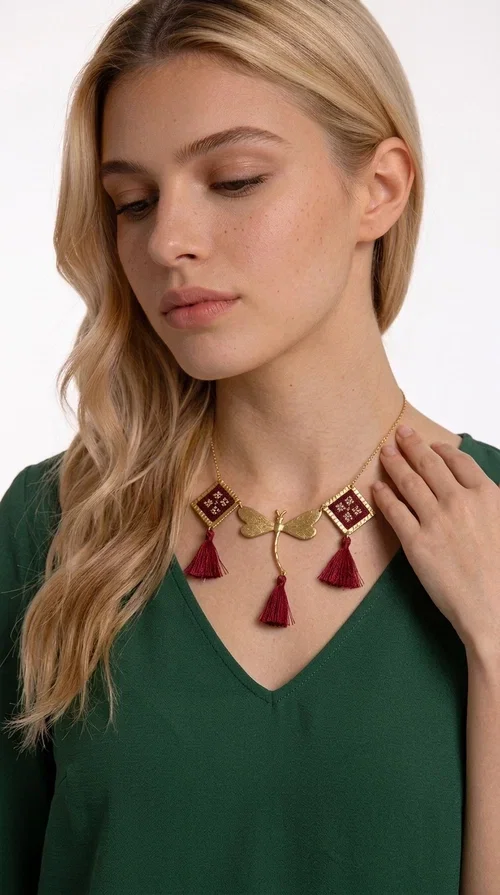 , The statement embroidered burgundy necklace is a jewel that instantly draws attention — featuring geometric patterns inspired by Greek folk art and a color palette that expresses richness and character. Designed by Greek Jewelry Designer Aikaterini Chalkiadaki, this handmade necklace combines gold-tone brass with embroidered fabric elements in deep burgundy, creating a result that balances between folk and contemporary style.

The necklace features two diamond-shaped pieces with embroidered geometric motifs, a central brass beetle-shaped link, and three burgundy tassels that add movement and drama to the overall look. The gold-tone brass chain completes the composition in an elegant, minimal way that lets the main elements shine. It is ideal as a statement piece for everyday looks as well as for evening occasions.

Wear it with a simple solid-colored shirt or dress to highlight its rich detail. It pairs exceptionally well with earthy tones, greens, and blacks.